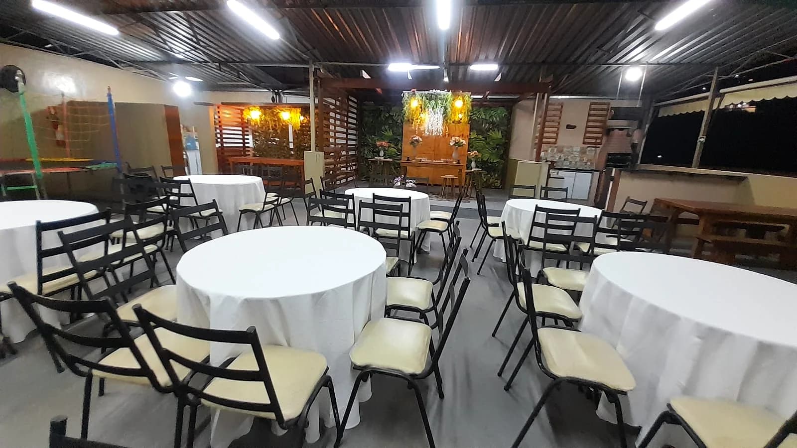 Salão preparado para recepção noturna com mesas brancas